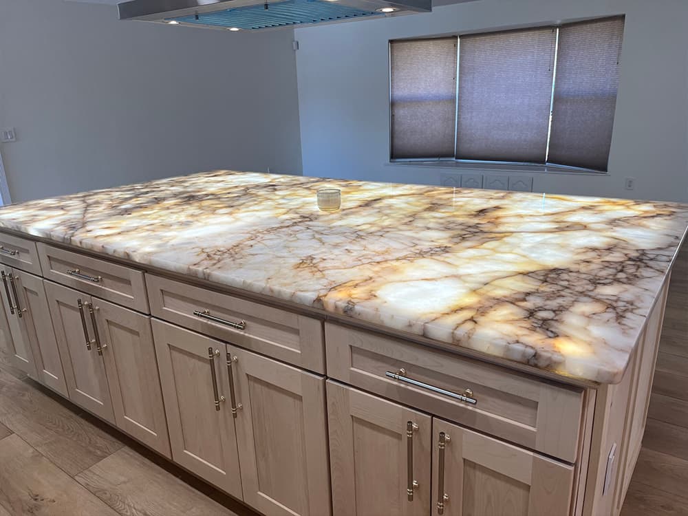 Backlit quartzite kitchen island glowing gold and cream with dramatic veining, on natural maple shaker cabinets