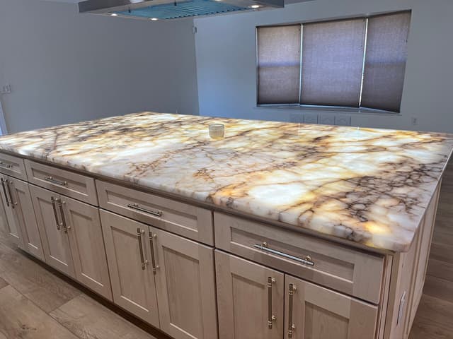 Backlit quartzite kitchen island glowing gold and cream, on natural maple shaker cabinets