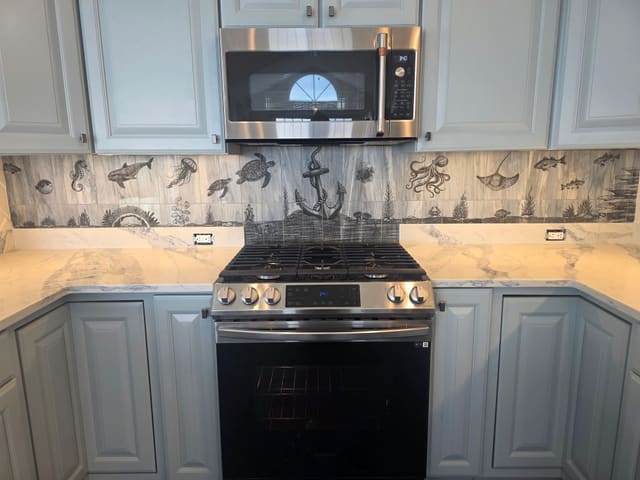Laser-etched seascape tile backsplash behind a range
