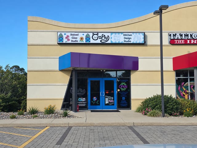 Storefront with a purple awning, blue doors and a sign reading Stained Glass Studio, Crafty, Kitchen Design Studio