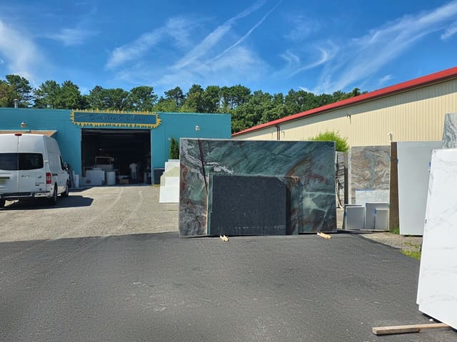 Rock Heads Granite Garden yard with stone slabs out front and the teal shop building with its open bay door