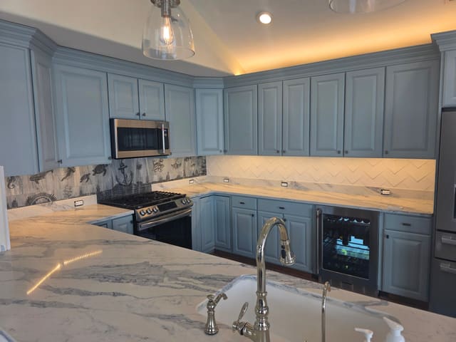 Finished kitchen install with blue cabinets, white quartz countertops and a laser-etched seascape backsplash