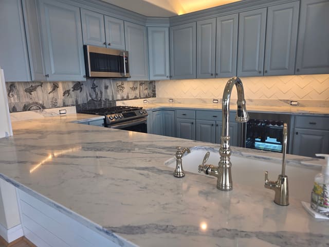 White Liraz quartz countertop with dramatic gray veining around an undermount sink, with blue cabinets and a herringbone backsplash beyond