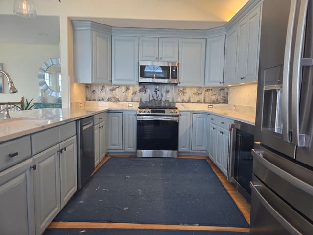 Etched sea-life backsplash running between blue cabinets and white veined countertops