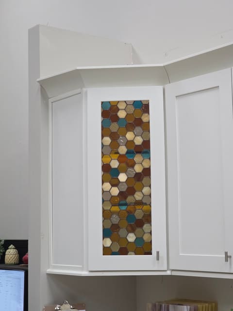 Honeycomb stained glass door set into a white corner cabinet between two plain shaker doors